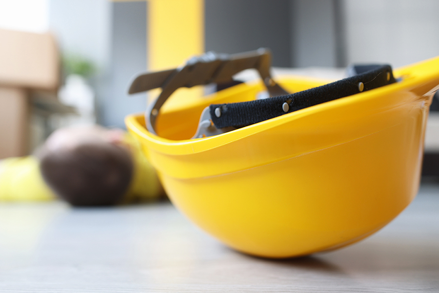 Slips, trips and falls, accident at work claim, yellow worker helmet on floor beside motionless construction worker. Accident during construction and renovation