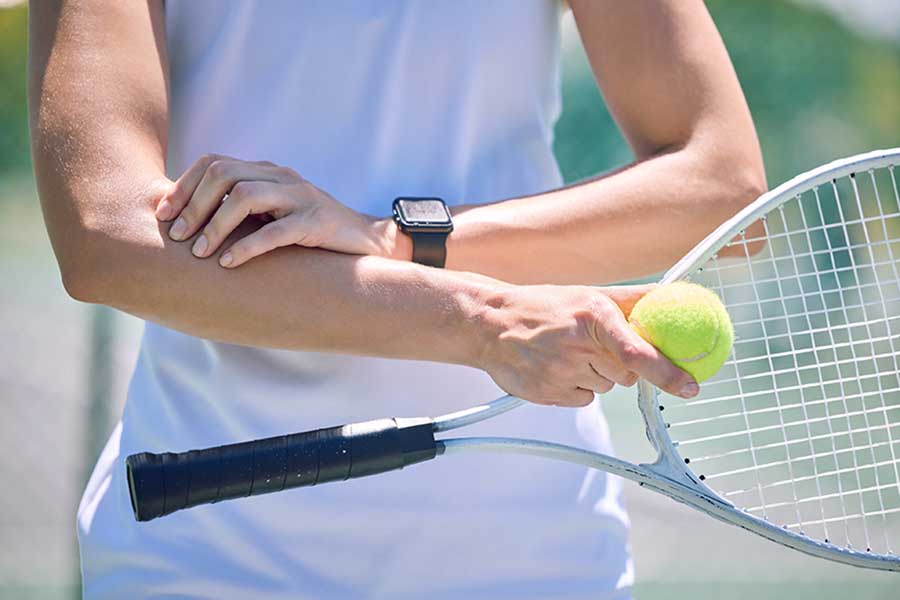 Sports injury claim, tennis player with a racket and ball standing on a court during for a match. Closeup of professional athlete with equipment touching a medical elbow injury