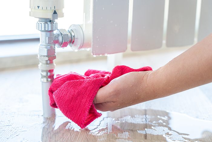 broken heating disrepair, female hand with rag cleaning water from heating radiator