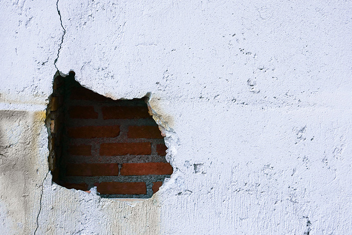 structural issue disrepair, hole in broken wall and old bricks on white background. Large crack on the wall of an old brick house, crumbling plaster and broken, cracked bricks.